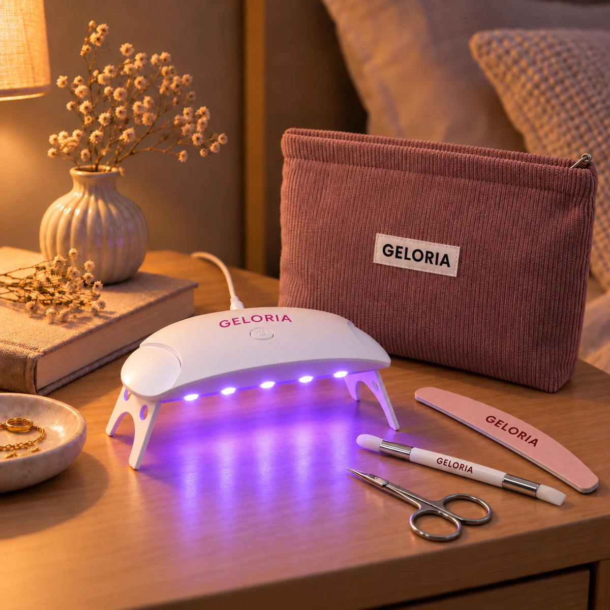 Lampe LED Geloria allumée sur une table de chevet, avec la trousse, la lime, le stylet et les ciseaux Geloria